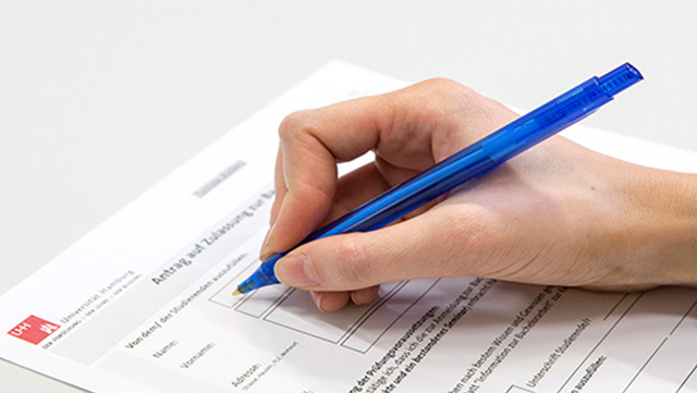 Rechte Hand mit blauem Kugelschreiber beim Ausfüllen eines Formulars