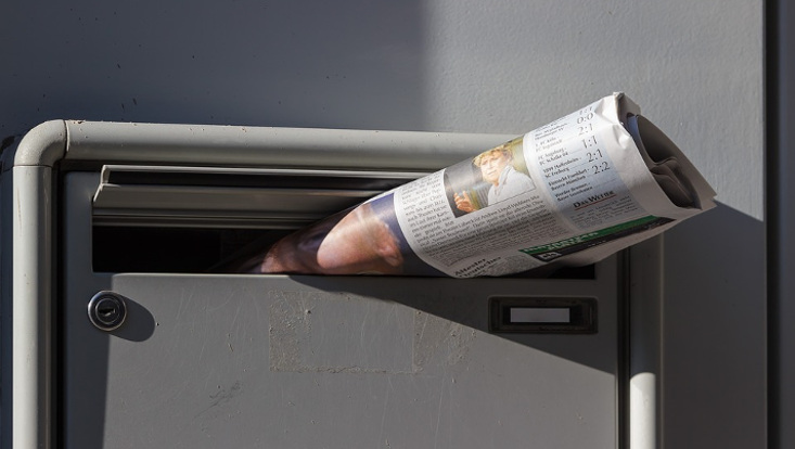 Zeitung guckt halb aus dem Briefkasten heraus.