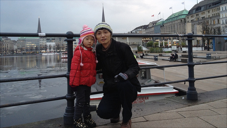 Fei Jie - Postdoc Mr Fei with his child in front of water and buildings in winter
