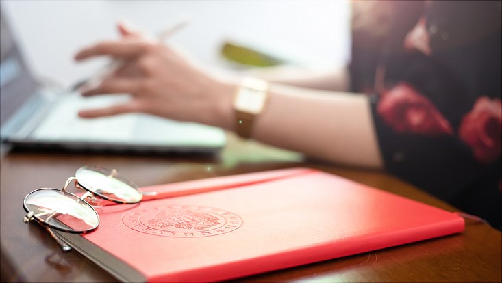 733x414-sun glasses lying on red notebook reflecting the bright sun while woman working on laptop in the background