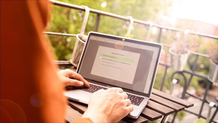 Mensch sitzt vor Laptop auf Balkon