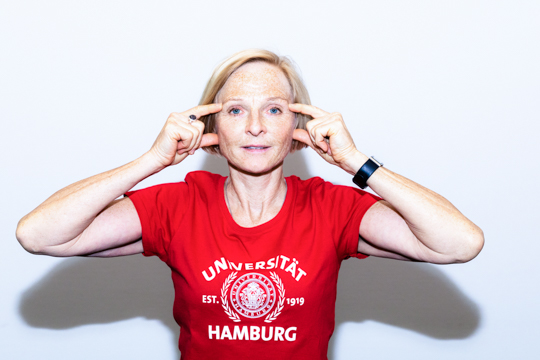 Eye relaxation exercise Smoothing out: A person has their hands next to the side of the face. Their thumbs and index fingers are extended. Their thumbs are just in front of their ears, and their index fingers are touching their temples.
