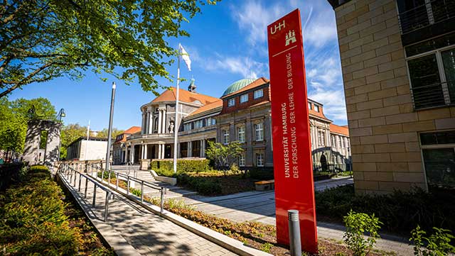 Das Hauptgebäude der Universität Hamburg im Sonnenschein. Im Vordergrund steht eine rote Säule