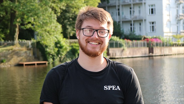 Portrait of Nicholas Box, former summer school participant, with water and trees in the background Portrait of Nicholas Box, former summer school participant, with water and trees in the background