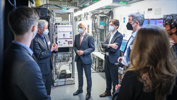 Eine Gruppe von Menschen steht in einem Gang. Im Hintergrund hängen Kabel und wissenschaftliche Geräte.
