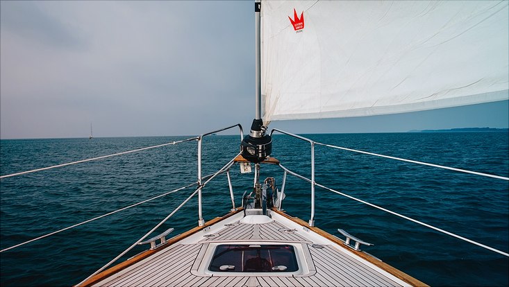 Es ist der Bug eines Segelschiffs auf dem Meer zu sehen, mit Blick in Fahrtrichtung auf das offene Meer.