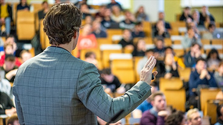 Rückenansicht eines Dozierenden im Hörsaal vor Studierenden
