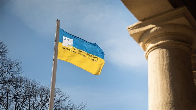 Die Flagge der Ukraine mit Logo der Universität Hamburg vor dem Hauptgebäude