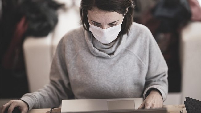 Frau mit Maske, die am Laptop arbeitet