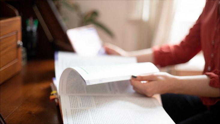 Eine junge Frau lernt am Schreibtisch mit einem aufgeschlagenen Buch und einem Tablet