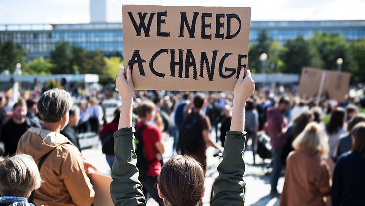 Frau, die ein Schild hält, auf dem steht "We need a change"