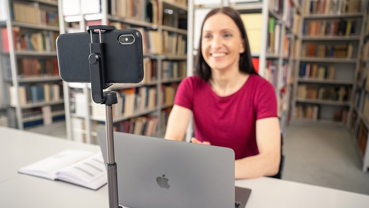 Frau sitzt vor Laptop und Kamera in Bibliothek