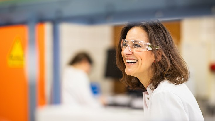 Frau mit Laborkittel und Schutzbrille lacht