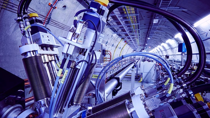 Das Bild zeigt den Tunnel des European XFEL bei Hamburg. Zu sehen ist ein Abschnitt des Teilchenbeschleunigers mit komplexer Hochtechnologie: Kabel, Rohre und Präzisionsgeräte verlaufen entlang der zentralen Beschleunigerstrecke.
