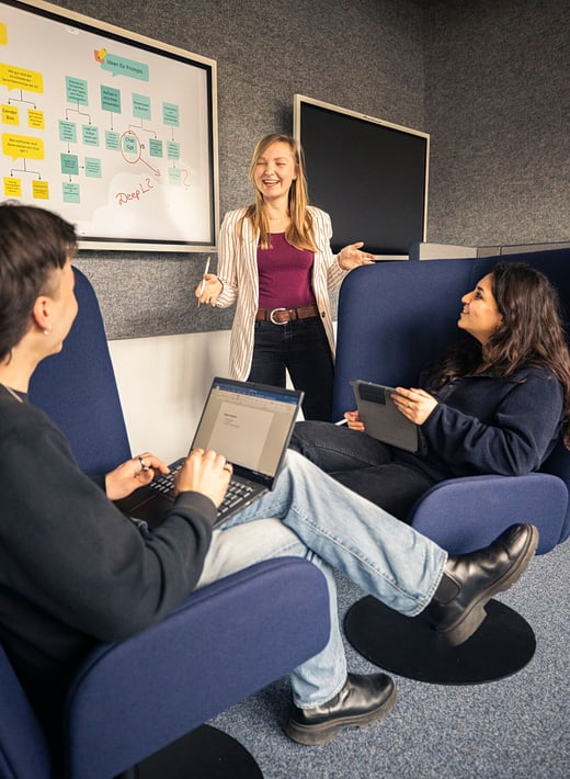 Drei junge Menschen im Gespräch mit Laptop und Whiteboard
