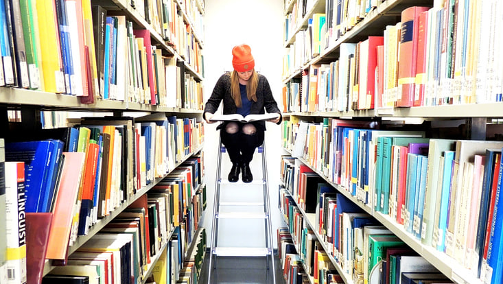 Frau sitzt in einer Bibliothek und liest