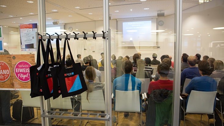 Blick durchs Fenster in einen Konferenzraum, in dem Personen einem Vortrag zuhören