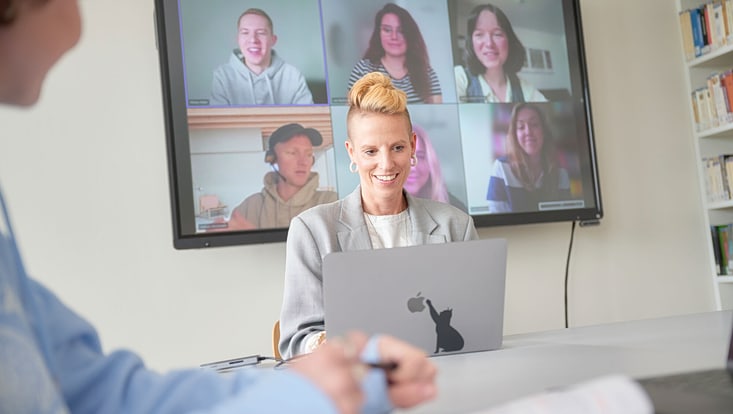 Foto aus einem Online-Seminar: eine Person im Vordergrund vor einem Notebook, im Hintergrund sind auf einem großen Monitor mehrere andere Personen zu sehen