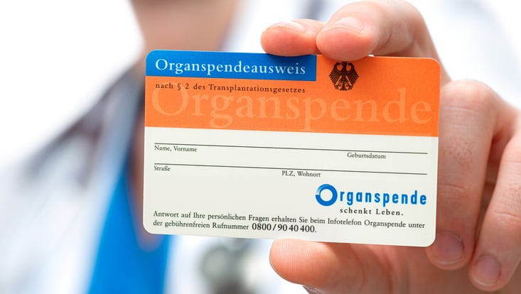 Ein orangefarbener Organspendeausweis, der in die Kamera gehalten wird.