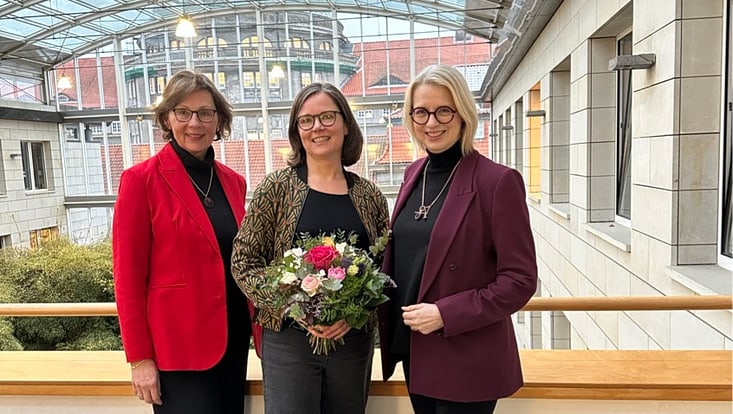 Die als stellvertretende Gleichstellungsbeauftragte wiedergewählte Dr. Uta Wagner trägt einen Blumenstrauß und wird von Dr. Angelika Paschke-Kratzin und Prof. Dr. Jetta Frost eingerahmt. Im Hintergrund das Foyer des Gebäudes ESA W.