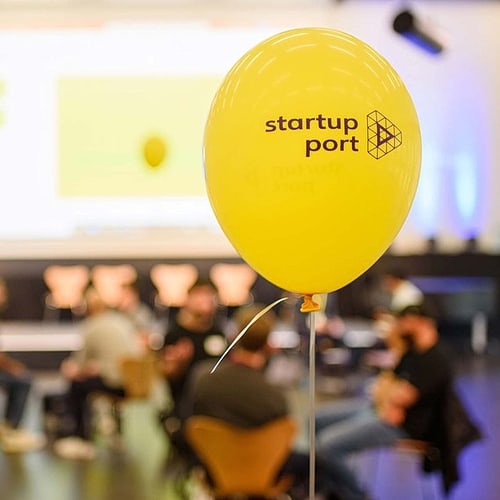 Gelber Luftballon mit dem Schriftzug "Startup Port", im HIntergrund Teilnehmende einer Veranstaltung