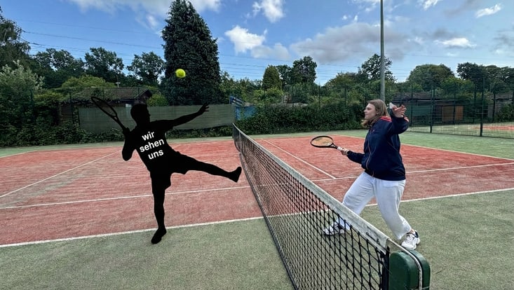 Eine Person und eine schwarze Silhouette spielen neben einem Tennisplatz Tennis