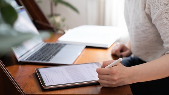 Symbolbild: Person mit Laptop und Tablet am Schreibtisch macht Notizen Symbolbild: Person mit Laptop und Tablet am Schreibtisch macht Notizen