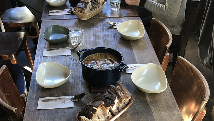 Holztisch mit leeren Schüsseln, Löffeln, ein Topf mit Suppe und Brot
