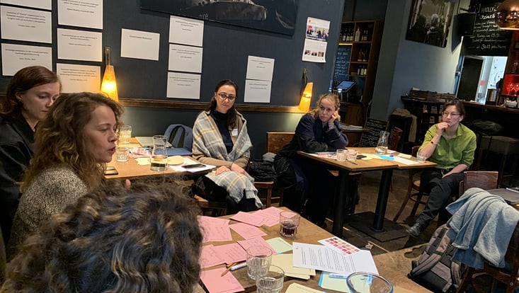 Personen sitzen an Tischen mit Arbeitsmaterialien