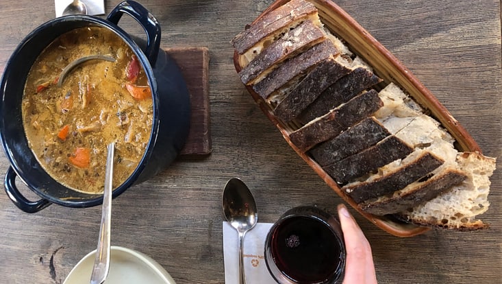 Topf mit Suppe und Schöpfer, Brot, eine Hand, die ein Glas umfasst