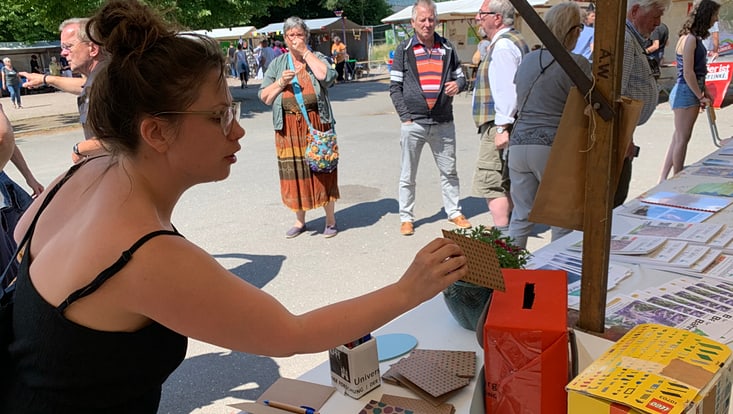 Eine Person wirft eine ausgefüllte Karte in eine Sammelbox an einem Informationsstand