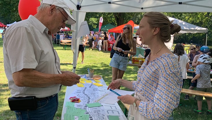Person erklärt einer anderen Person etwas an einem Informationsstand