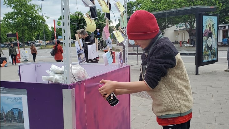 Kind sprüht Informationsstand mit Spraydose rosa an