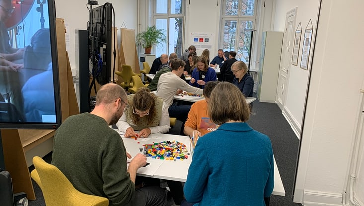 04-03-koord-transferfonds-slider-2024-03-2024-11-27-transferfonds24-kick-off-cucaser(14)-733x414 Personen sitzen an Tischen und bauen etwas mit Legosteinen