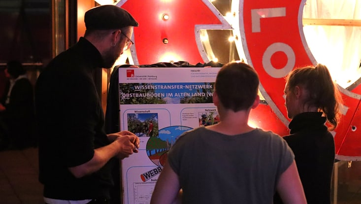 04-04-expertise-transferfonds-6-20241008-apcsutransferfonds-cfmoeller-57-733x414 Drei Personen betrachten ein Poster mit der Überschrift „Wissenstransfer-Netzwerk – Obstbauböden im Alten Land“