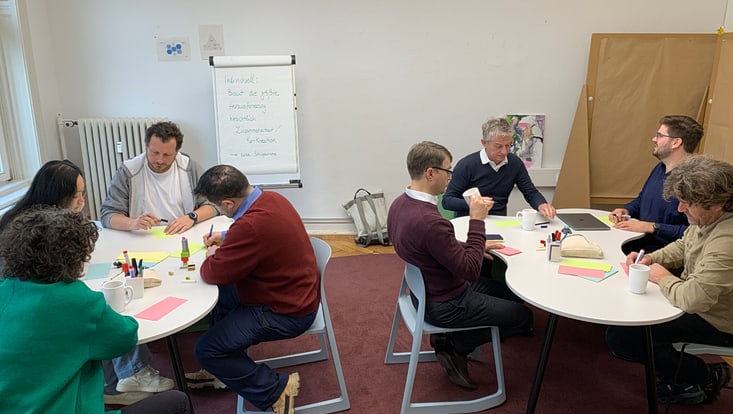20251125-tf-kick-off-cucaser-(25)-733x414 Einige Personen sitzen an zwei verschiedenen Tischen in einem Raum und schreiben auf Karteikarten