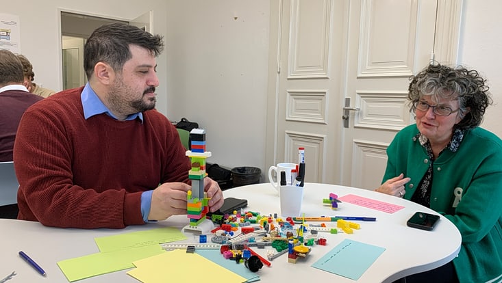20251125-tf-kick-off-cucaser-(32)-733x414 Zwei Personen sitzen an einem Tisch mit Lego Installation