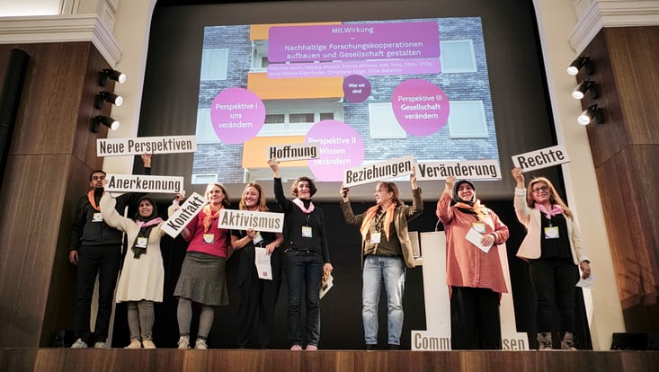 Teilnehmende des Forum Citizen Science auf einer Bühne halten Schilder mit den Aufschriften Anerkennung, Neue Perspektiven, Aktivismus, Kontakt, Hoffnung, Beziehungen, Veränderung