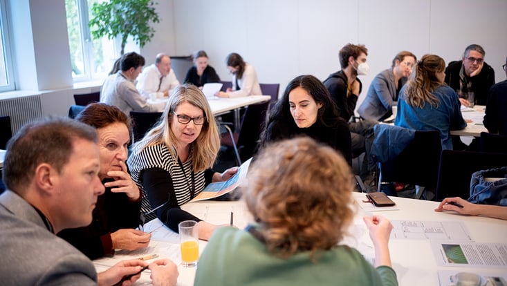 Personen sitzen an Tischen bei einem Workshop und unterhalten sich