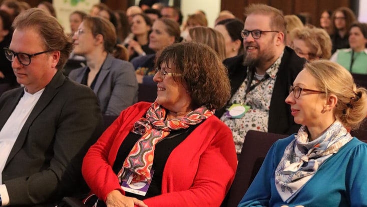 Lächelnde Personen sitzen in einem Publikum