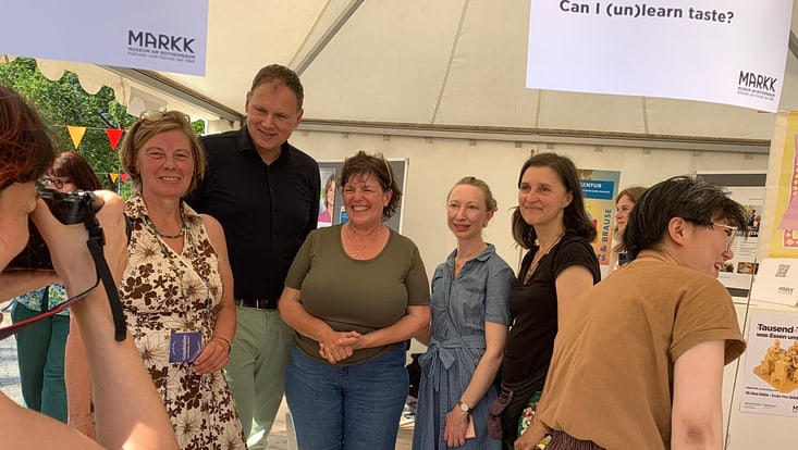 02-05-vernetzung-festivals-slider-campusfest-733x414 Lächelnde Personen stehen vor einem Informationsstand und werden von einer Person mit Kamera fotografiert
