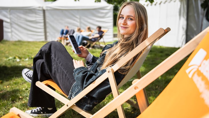 Eine Studierende sitzt auf einer Liege und hat ein Handy in der Hand.