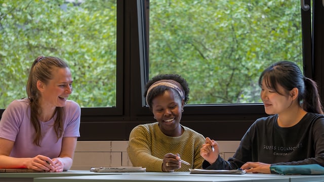 Drei Studentinnen sitzen lachend an einem Tisch.