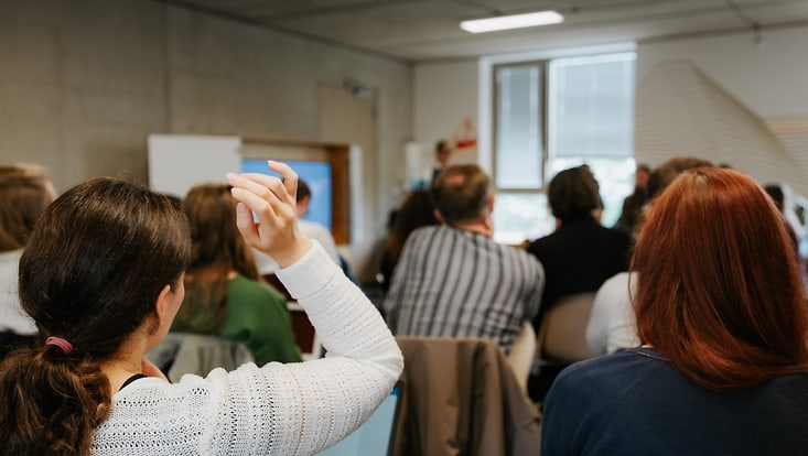 Foto von Personen in einer Vortragssituation, die nur von hinten zu sehen sind