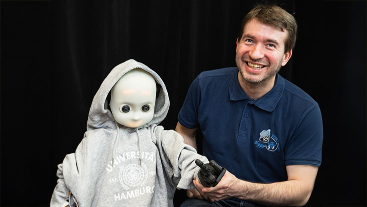Dr. Matthias Kerzel Mann mit hellbraunen Haaren sitzt neben einem Roboter
