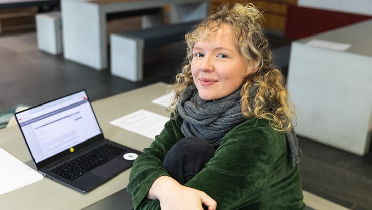 Eine Studierende sitzt an einem Schreibtisch. Auf dem Schreibtisch befindet sich ein Laptop.