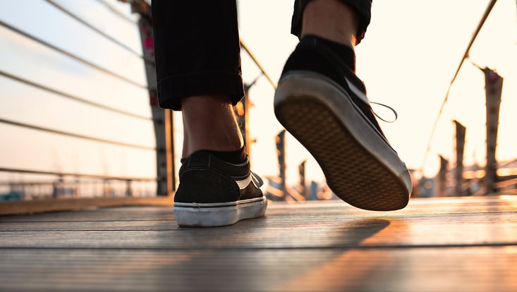 Die Schuhe einer Person sind zu sehen, die auf einer Brücke geht.