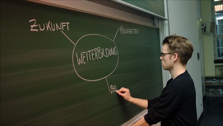 Ein Student schreibt das Wort Weiterbildung an die Tafel