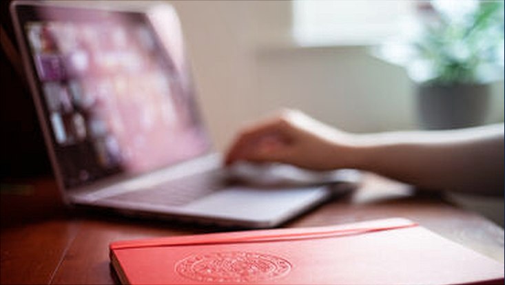 Ein Notizbuch vor einem Laptop mit einem ZoomCall darauf.
