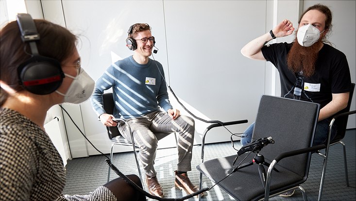 Zwei Teilnehmende testen zusammen mit Michael Büker Kopfhörer und Mikrofon während seines Workshops